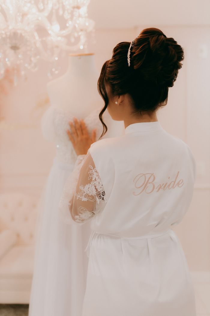 about-us Bride in a white robe admiring wedding gown. Bridal preparation moments.